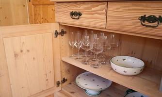 A wooden cabinet with open doors, showcasing glasses and dishes. In the lower compartment, several glasses and a bowl are visible.