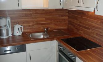 A modern kitchen with wooden decor and white cabinets. It is well-equipped with a stove, a sink, and a kettle.