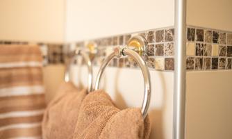 Brown towels are hanging on a stylish towel holder. In the background, a decorative tile border is visible.