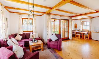A friendly living room with red-purple sofas and wooden beams. The room has large windows and an adjacent dining area.