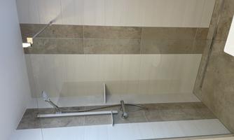 A modern shower cubicle with a glass partition and simple, light tiles. The space appears clean and well-designed.