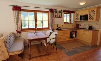 A cozy kitchen with wooden cabinets and a dining table. Large windows let in plenty of light and offer a view of nature.