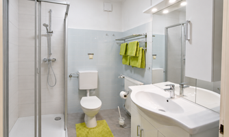 A modern bathroom with a shower, a sink, and a toilet. The decor is bright and friendly, with towels