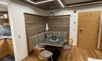 A cozy dining area with a wooden bench and a table. The walls are made of wood, and a beautiful chandelier hangs from the ceiling.