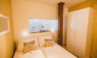 A cozy bedroom with a double bed and modern pillows. The room has a bright color scheme and a view of an open kitchen.