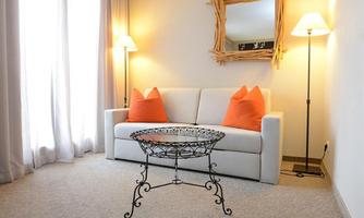 A cozy living room with a white sofa and orange cushions. An elegant table and soft light create an inviting atmosphere.