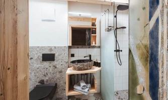 A modern bathroom with wood and stone elements. There is a glass shower wall, a stone sink, and towels on a shelf.