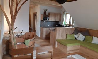 A modern living room with a cozy seating area and a wood stove. The kitchen is open and invites for sociable cooking.