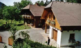 Two charming wooden houses surrounded by green landscape. The buildings are adorned with flowers and offer a cozy atmosphere.
