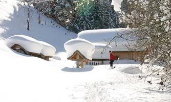 A winter landscape with snow-covered huts and a hiker. The sky is clear and the environment is calm and idyllic.