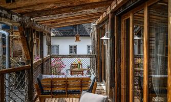 A cozy balcony with wooden furniture and a view of a pretty house. Blooming plants adorn the surroundings and create an inviting atmosphere.