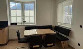 A modern dining room with a wooden table and comfortable black chairs. Large windows provide plenty of natural light and offer a view outside.