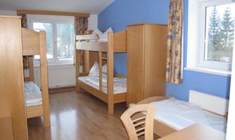 A simple room with two bunk beds and a table. The walls are blue, and there is plenty of daylight coming through the window.