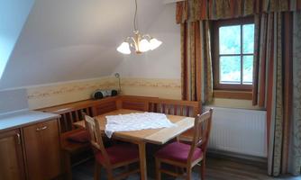 A cozy dining area with a wooden table and chairs. The walls are light and decorated with curtains, and a window lets natural light shine in.