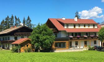 A picturesque farmhouse with a red roof amidst lush green meadows. Surrounded by trees and blue sky, the scene exudes tranquility and coziness.