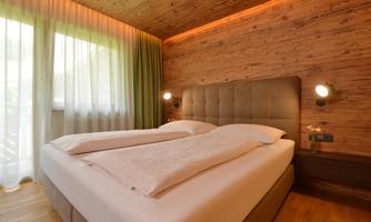 A modern bedroom with two beds and wooden walls. Large windows provide plenty of daylight and a cozy atmosphere.
