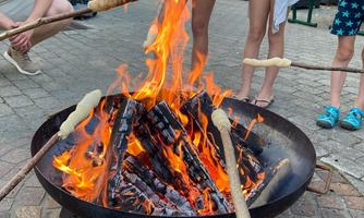 A campfire with flaming logs and several people roasting dough rolls over the fire. The atmosphere is cozy and inviting.