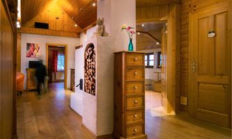 A bright hallway in a wooden house with light wooden flooring. At the end of the hallway stands a fireplace and a dresser.