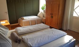 A bright room with a large bed and an additional sleeping option. There is a wooden wardrobe and daylight streaming through the windows.