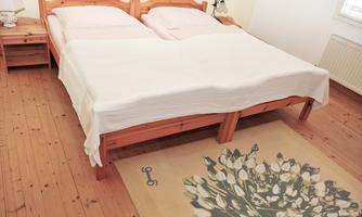 A cozy bedroom with a double bed and a wooden floor. The carpet features a floral design and creates an inviting atmosphere.