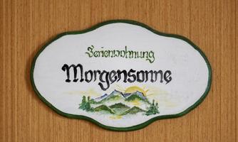 A sign with the inscription "Holiday Apartment Morning Sun". The image shows a picturesque landscape with mountains and a rising sun.