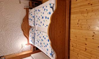 A cozy wooden double bed with floral bedding. The floor is made of light wood and the walls are plain.