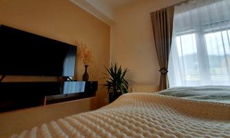 A cozy bedroom with a television on the wall and a window that provides natural light. The decor is modern and inviting.