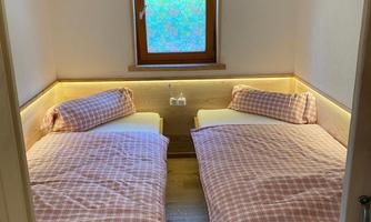 A cozy bedroom with two single beds and wooden furniture. The window lets in natural light and creates an inviting atmosphere.