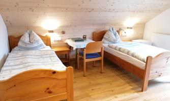 A cozy bedroom with two wooden beds and a small seating area. The walls are light, and the wood creates a warm atmosphere.