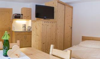 A cozy room with wooden furniture and a television. In the corner, there is a small kitchenette and a dining table.