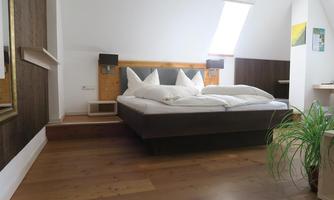 A modern bedroom with a large double bed and white pillows. It has wood-colored walls and a bright, inviting space.