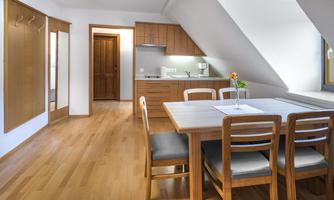 A modern kitchen with a dining table and four chairs. The room has large windows and bright wooden surfaces.