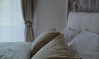 A cozy bedroom with soft cushions and a large window. The curtains are bright and the room feels friendly and welcoming.