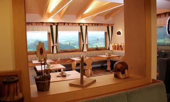 An inviting restaurant with wooden decor and a beautiful view of the landscape. The windows are generously lit, creating a cozy atmosphere.