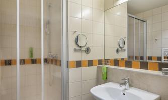 A modern bathroom with a shower and a sink. The walls are brightly tiled and there is a large mirror.