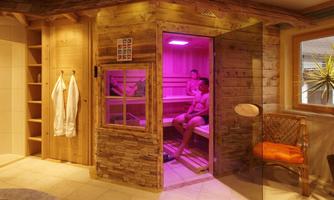 A cozy wooden sauna with soft pink light. Inside, several people relax on the benches.