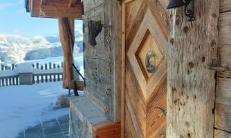 A rustic wooden door on a chalet-like building. In the background, snow-covered mountains and a clear sky can be seen.