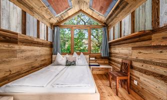 A cozy bedroom with wooden walls and a large window front. The room is simply furnished and offers a view of greenery.