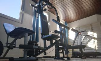 A home gym with various workout equipment. In the background, there are windows that let in daylight.