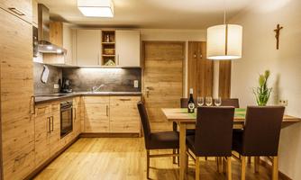 A modern kitchen with wooden cabinets and a dining area. The space is well-lit and cozily furnished.