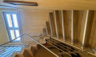 A wooden staircase with a modern stainless steel railing. The room is bright and adorned with wood paneling.