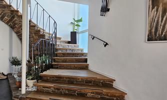 A modern staircase with wooden steps and an elegant railing. There is a plant and a piece of art on the wall.