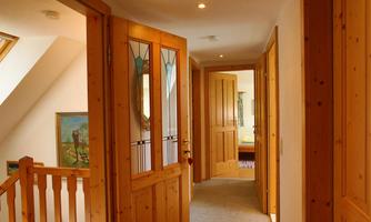 A bright hallway with wooden doors and carpeted floor. On the right is a room with a view of a painting.