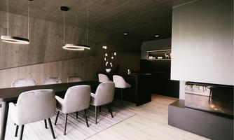 A modern dining room with an elegant table and stylish chairs. The walls are made of exposed concrete, and there is a cozy fireplace.