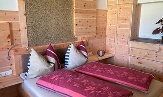 A cozy bedroom with a double bed and red pillows. The walls are made of light wood, creating a warm atmosphere.