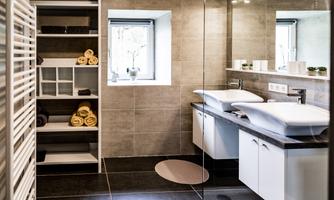 A modern bathroom with two sinks and a large mirror. The shelves are decorated with towels and cosmetics.