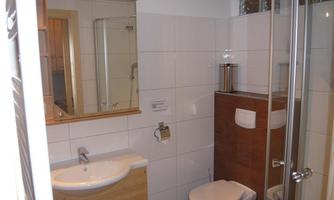 A modern bathroom with a shower, sink, and toilet. The walls are brightly tiled and there is a large mirror.