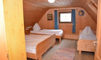 A cozy room with wooden paneling. There are two single beds, a carpet, and windows with blue curtains.