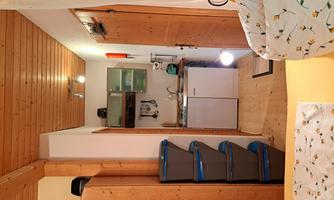A small kitchenette with wooden shelves and a refrigerator. The room has a cozy atmosphere with a view of a sleeping area.