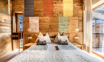 A cozy bedroom with wood paneling and colorful wall panels. The bed is adorned with soft pillows and a warm blanket.